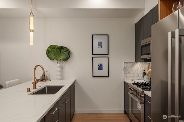 kitchen with appliances with stainless steel finishes, pendant lighting, sink, decorative backsplash, and light stone countertops