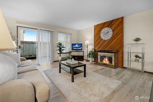 living room with a brick fireplace, a textured ceiling, and light hardwood / wood-style flooring