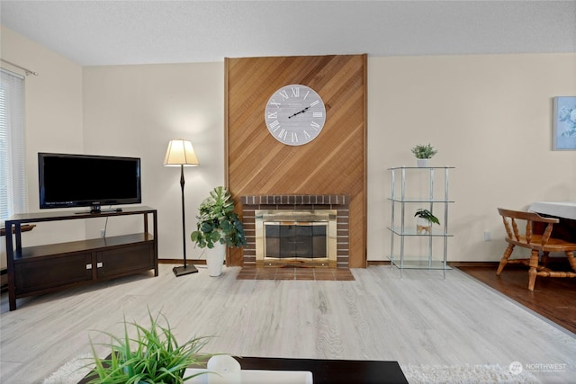 living room with a textured ceiling, a brick fireplace, and light wood-type flooring