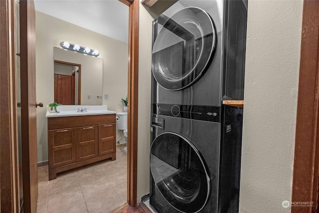 clothes washing area with light tile patterned floors, sink, and stacked washer / dryer