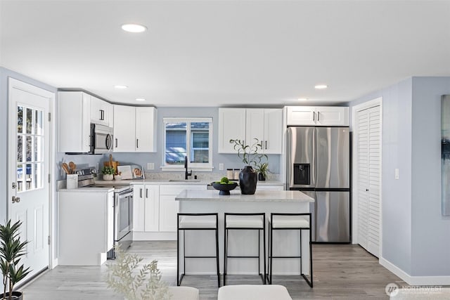 kitchen with sink, a breakfast bar area, white cabinetry, stainless steel appliances, and a center island