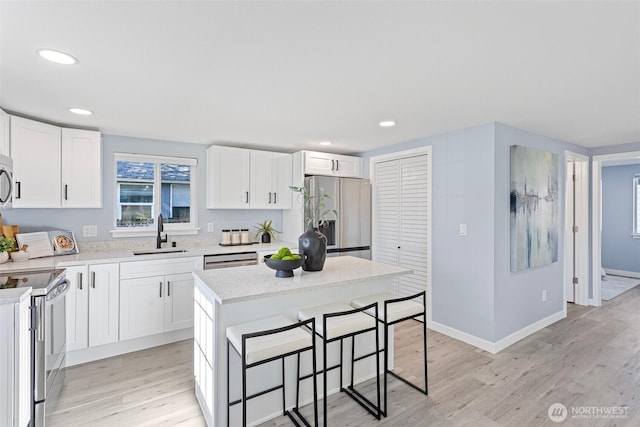 kitchen with white cabinetry, sink, stainless steel appliances, and a kitchen island