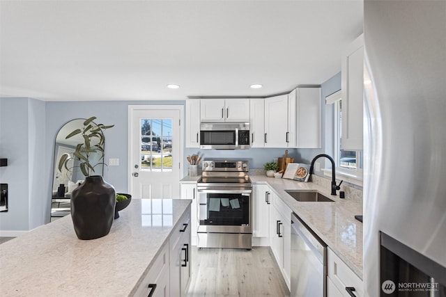 kitchen featuring sink, light hardwood / wood-style flooring, appliances with stainless steel finishes, light stone countertops, and white cabinets