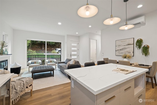 kitchen with a wall mounted air conditioner, decorative light fixtures, a center island, hardwood / wood-style floors, and white cabinets