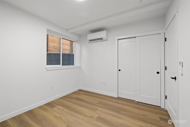 unfurnished bedroom featuring a wall mounted AC, light hardwood / wood-style floors, and a closet