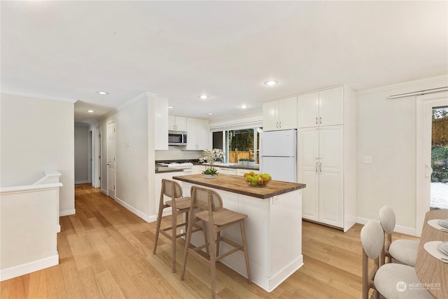 kitchen featuring butcher block countertops, a breakfast bar, white cabinets, and white refrigerator