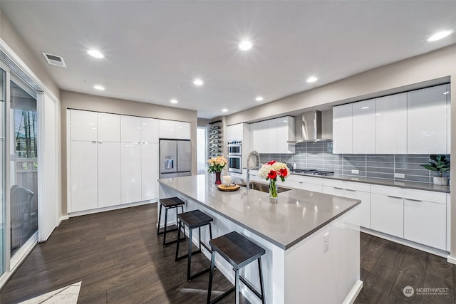 kitchen featuring white cabinetry, sink, a kitchen breakfast bar, a center island with sink, and wall chimney exhaust hood