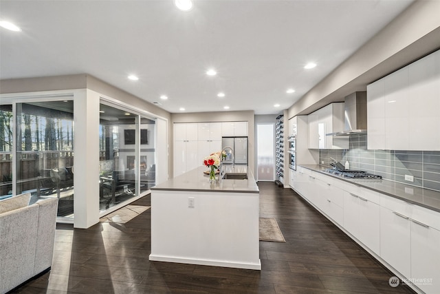 kitchen with a center island with sink, wall chimney range hood, dark hardwood / wood-style flooring, stainless steel appliances, and white cabinets