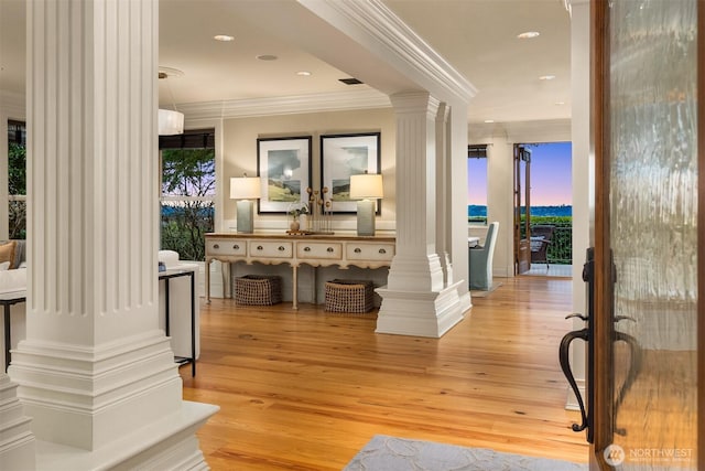 hall with ornamental molding, light wood-type flooring, a healthy amount of sunlight, and decorative columns