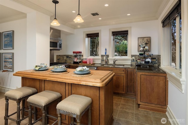 kitchen with pendant lighting, sink, crown molding, backsplash, and a kitchen bar