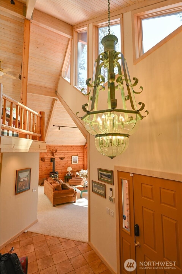 tiled entryway featuring carpet flooring, wooden ceiling, a high ceiling, wooden walls, and a wood stove
