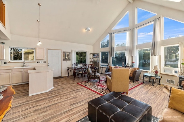 living area featuring light wood finished floors, visible vents, and high vaulted ceiling