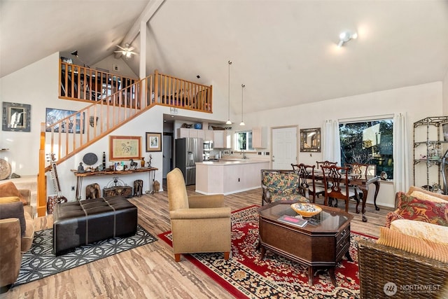 living room featuring light wood finished floors, stairway, high vaulted ceiling, and baseboards