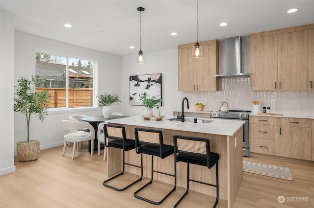 kitchen featuring sink, stainless steel electric range, a kitchen island with sink, hanging light fixtures, and wall chimney exhaust hood