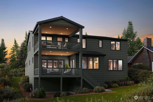 back house at dusk featuring a lawn and a balcony