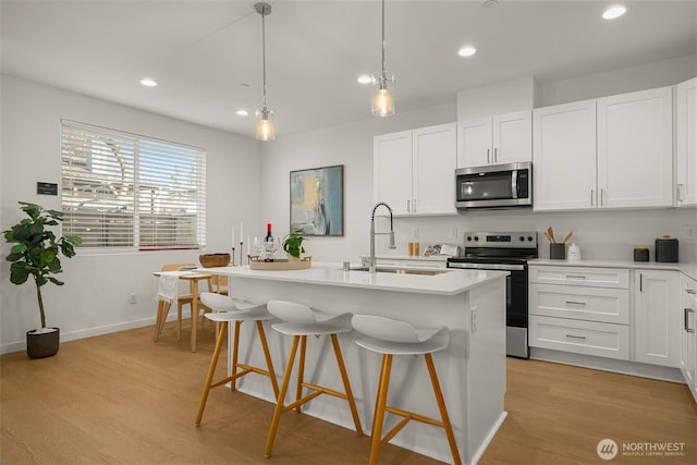 kitchen with stainless steel appliances, a sink, light wood-style flooring, and a breakfast bar area