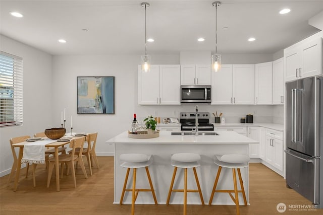 kitchen featuring stainless steel appliances, light wood-type flooring, light countertops, and a breakfast bar area