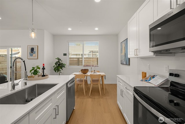 kitchen with appliances with stainless steel finishes, light wood-type flooring, light countertops, and a sink