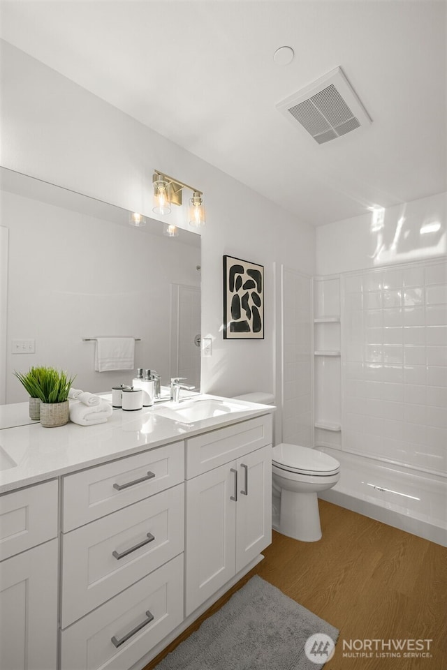 bathroom featuring visible vents, toilet, a sink, a tile shower, and wood finished floors