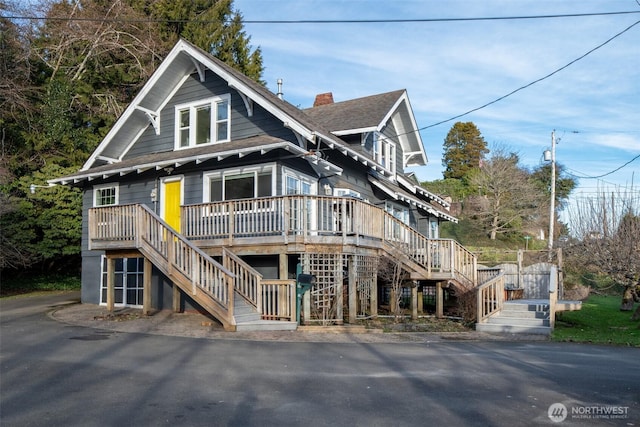 view of front facade featuring a shingled roof, stairs, a chimney, and a wooden deck