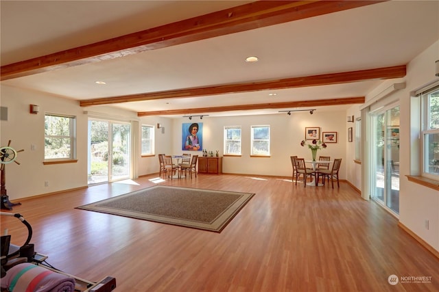 unfurnished living room with beam ceiling, a wealth of natural light, and light wood-type flooring