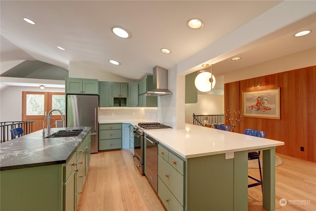 kitchen featuring sink, green cabinets, stainless steel appliances, a kitchen bar, and wall chimney exhaust hood