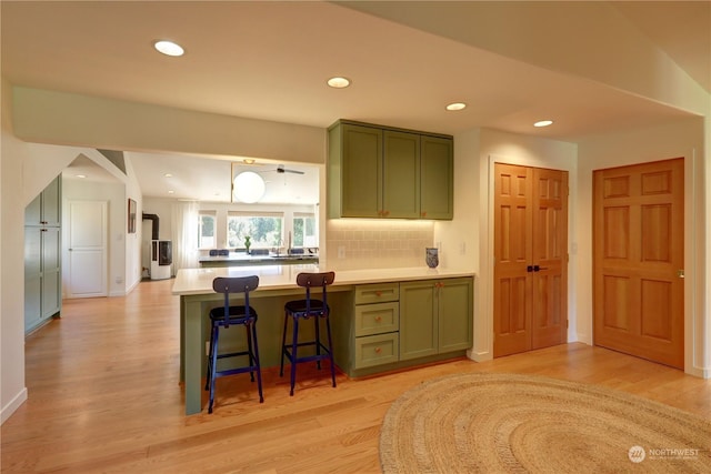 kitchen with tasteful backsplash, a breakfast bar, green cabinets, and light wood-type flooring