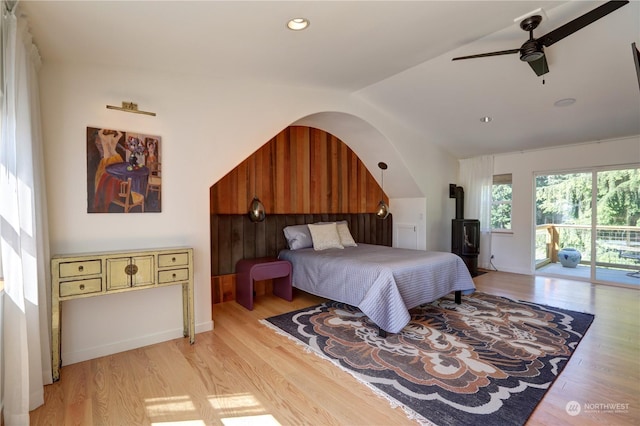 bedroom with lofted ceiling, light hardwood / wood-style flooring, a wood stove, ceiling fan, and access to exterior