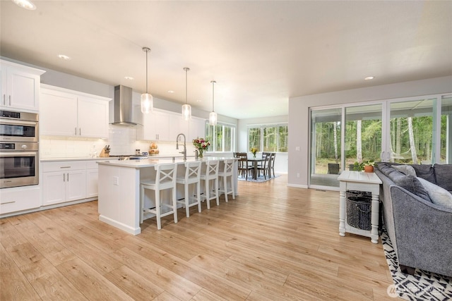 kitchen with appliances with stainless steel finishes, wall chimney exhaust hood, hanging light fixtures, and white cabinets