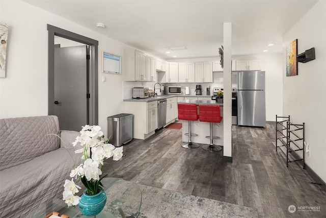 kitchen featuring appliances with stainless steel finishes, dark wood-type flooring, white cabinets, and a kitchen breakfast bar