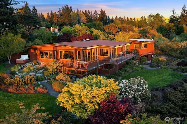 back house at dusk featuring a wooden deck, a yard, and a hot tub