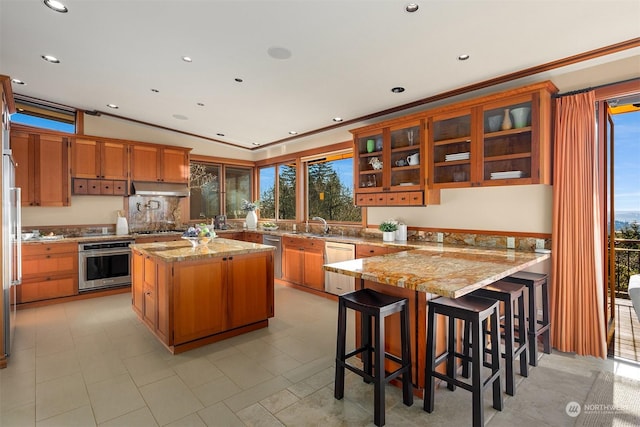 kitchen with a kitchen island, appliances with stainless steel finishes, light stone counters, and a kitchen breakfast bar