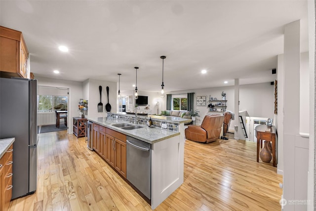 kitchen with appliances with stainless steel finishes, light wood-type flooring, light stone counters, pendant lighting, and sink