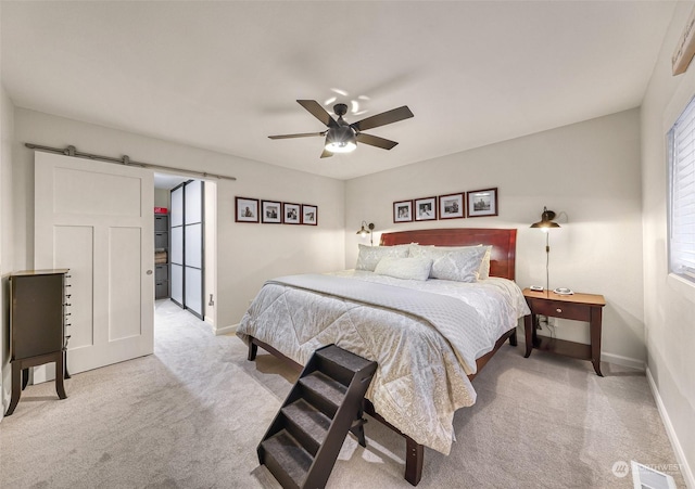 bedroom with ceiling fan, light colored carpet, and a barn door