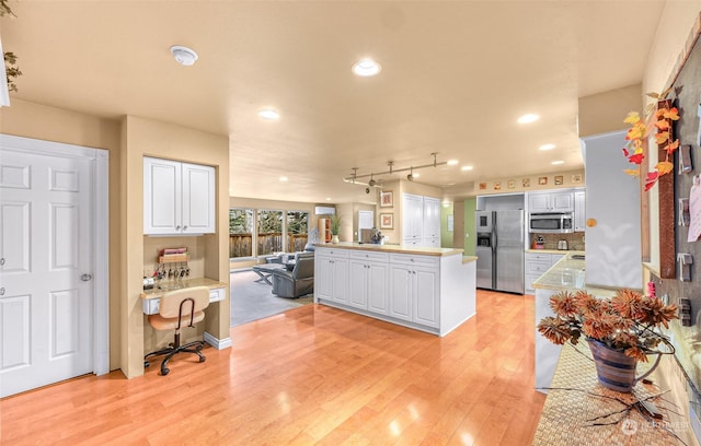 kitchen with built in desk, white cabinetry, kitchen peninsula, stainless steel appliances, and light hardwood / wood-style flooring