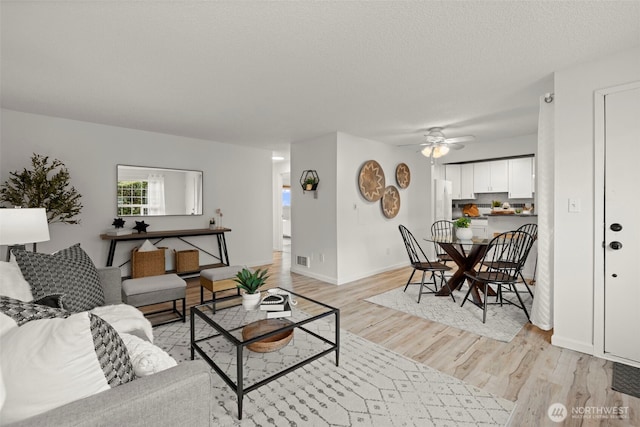 living room with ceiling fan, light hardwood / wood-style floors, and a textured ceiling