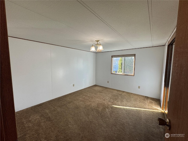 spare room with carpet flooring, an inviting chandelier, and a textured ceiling