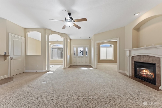 unfurnished living room featuring ceiling fan, light colored carpet, decorative columns, and a tile fireplace