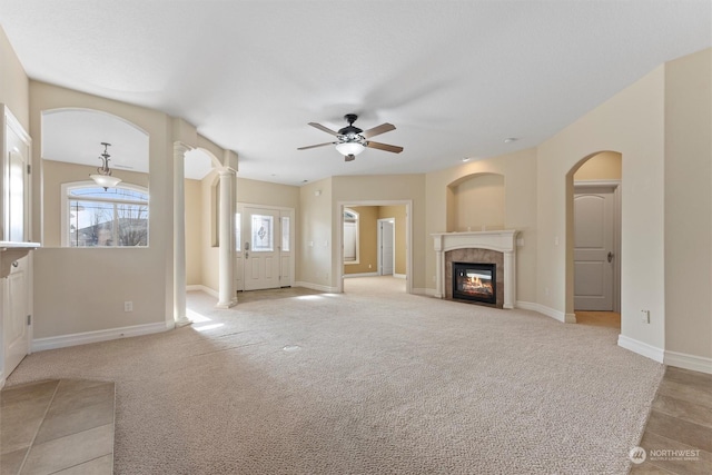 unfurnished living room with ceiling fan, light colored carpet, a premium fireplace, and decorative columns