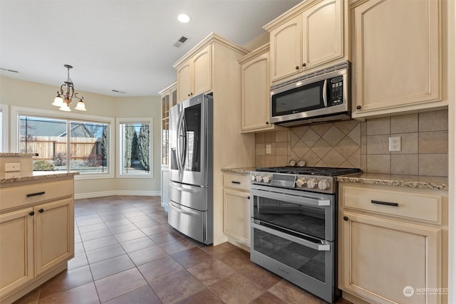 kitchen featuring appliances with stainless steel finishes, decorative light fixtures, dark tile patterned flooring, backsplash, and light stone countertops