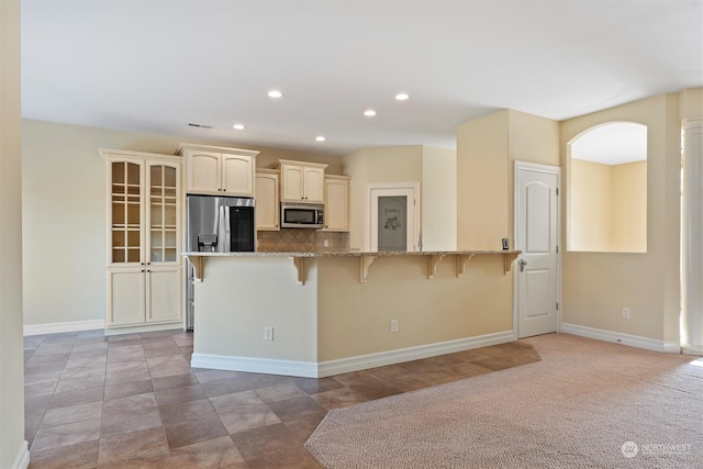 kitchen featuring stone counters, appliances with stainless steel finishes, a kitchen bar, decorative backsplash, and cream cabinets