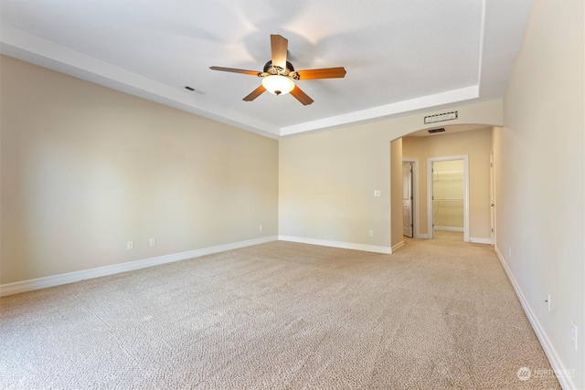 unfurnished room featuring a raised ceiling, light colored carpet, and ceiling fan