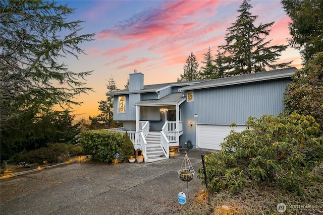 bi-level home featuring driveway, an attached garage, a chimney, and a porch