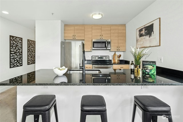 kitchen with appliances with stainless steel finishes, dark stone countertops, a breakfast bar area, kitchen peninsula, and light brown cabinets