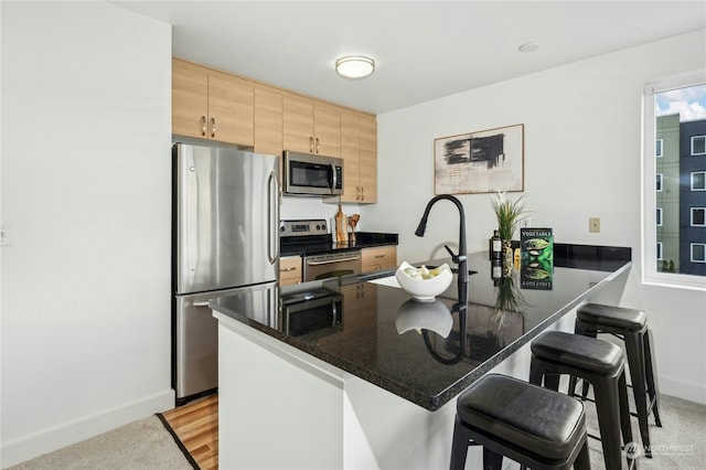 kitchen featuring sink, a kitchen bar, dark stone counters, kitchen peninsula, and stainless steel appliances