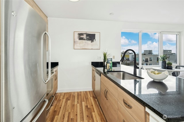 kitchen featuring light brown cabinetry, sink, light wood-type flooring, appliances with stainless steel finishes, and dark stone counters