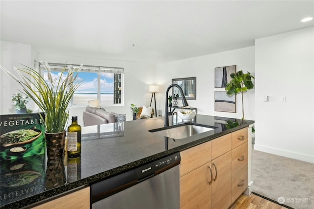 kitchen with stainless steel dishwasher, dark stone counters, light brown cabinetry, and sink