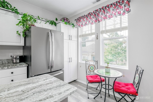 kitchen with light stone counters, stainless steel fridge, light hardwood / wood-style flooring, and white cabinets