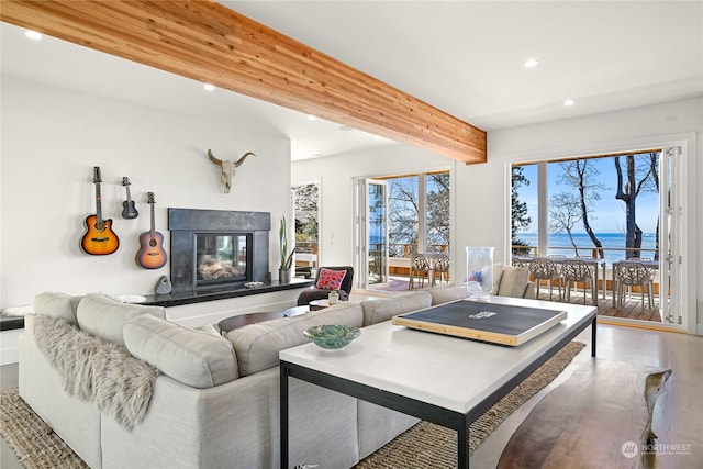 living room featuring beamed ceiling, recessed lighting, a water view, a glass covered fireplace, and plenty of natural light