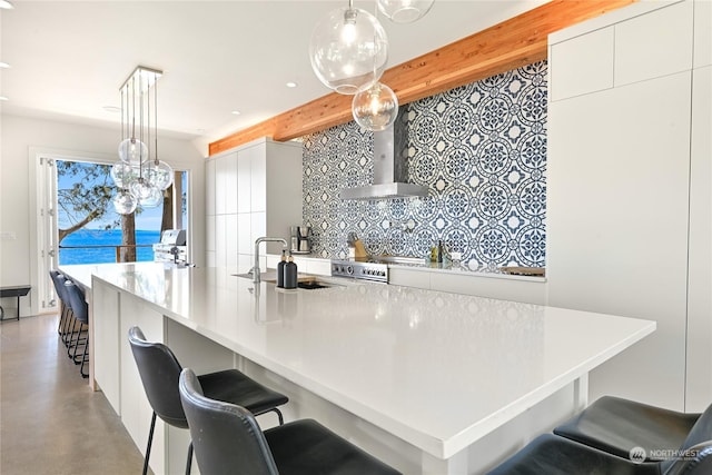 kitchen with light countertops, hanging light fixtures, a sink, wall chimney range hood, and modern cabinets